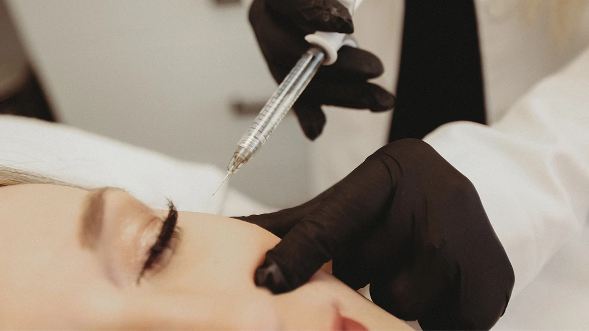 A woman receiving eyebrow shaping from a doctor in a clinical setting. A woman receiving eyebrow shaping from a doctor in a clinical setting.
