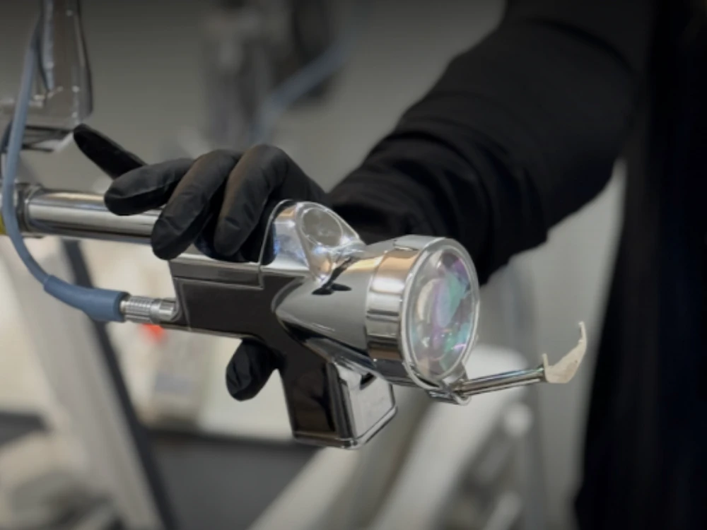 A person wearing black gloves is holding a chrome dental tool with a nozzle and transparent cover, in a clinical setting. The atmosphere is professional. A person wearing black gloves is holding a chrome dental tool with a nozzle and transparent cover, in a clinical setting. The atmosphere is professional.