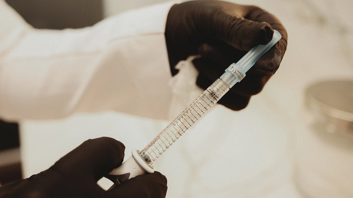 A healthcare professional in a white coat holds a syringe, preparing for a medical procedure or vaccination. A healthcare professional in a white coat holds a syringe, preparing for a medical procedure or vaccination.