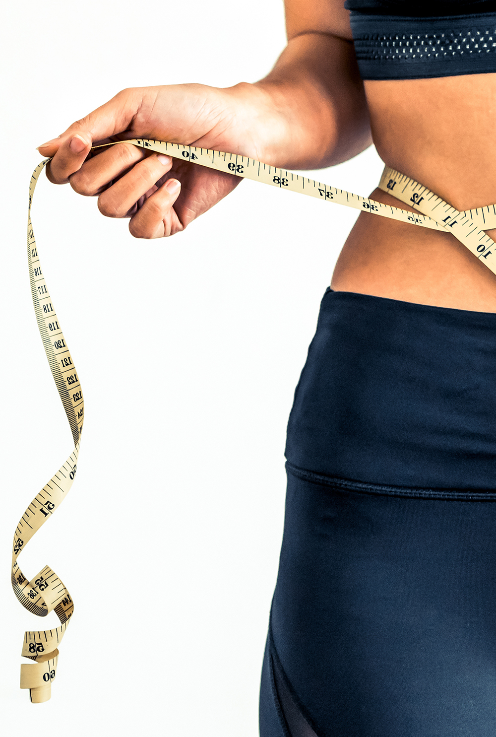 A person in workout attire wraps a measuring tape around their waist, indicating fitness or weight loss focus. The mood is determined and focused.